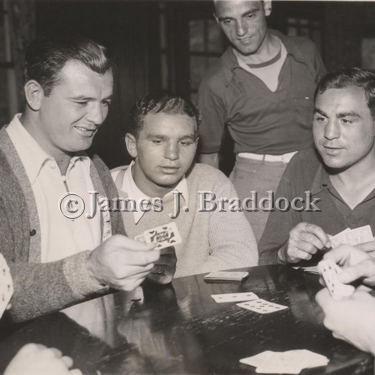 After a day of strenuous training at his camp in Kenosha, Wiss., champion Jim Braddock takes on his sparring mates once more - but this time in a friendly card game. Left to right: Jim Braddock, Henry Copper, and Charlie Massera. Standing is Sam Milton.